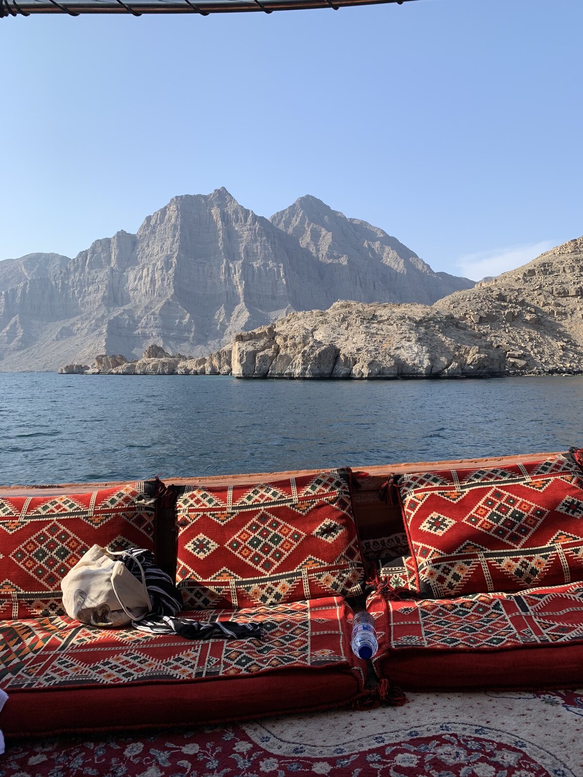 Red woven floor cushions facing the water and mountains of Musandam, Oman