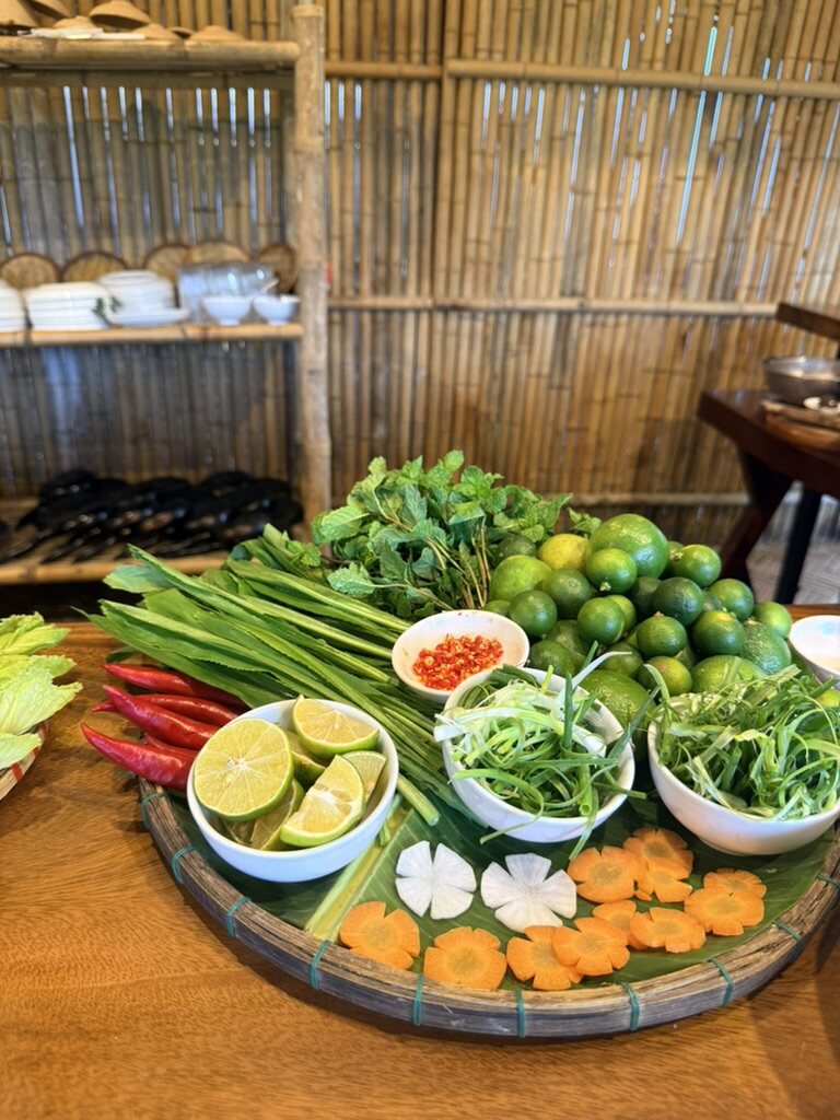 Fresh herbs, limes and chilies laid out on a woven tray at a family-run cooking class in Hoi An, Vietnam